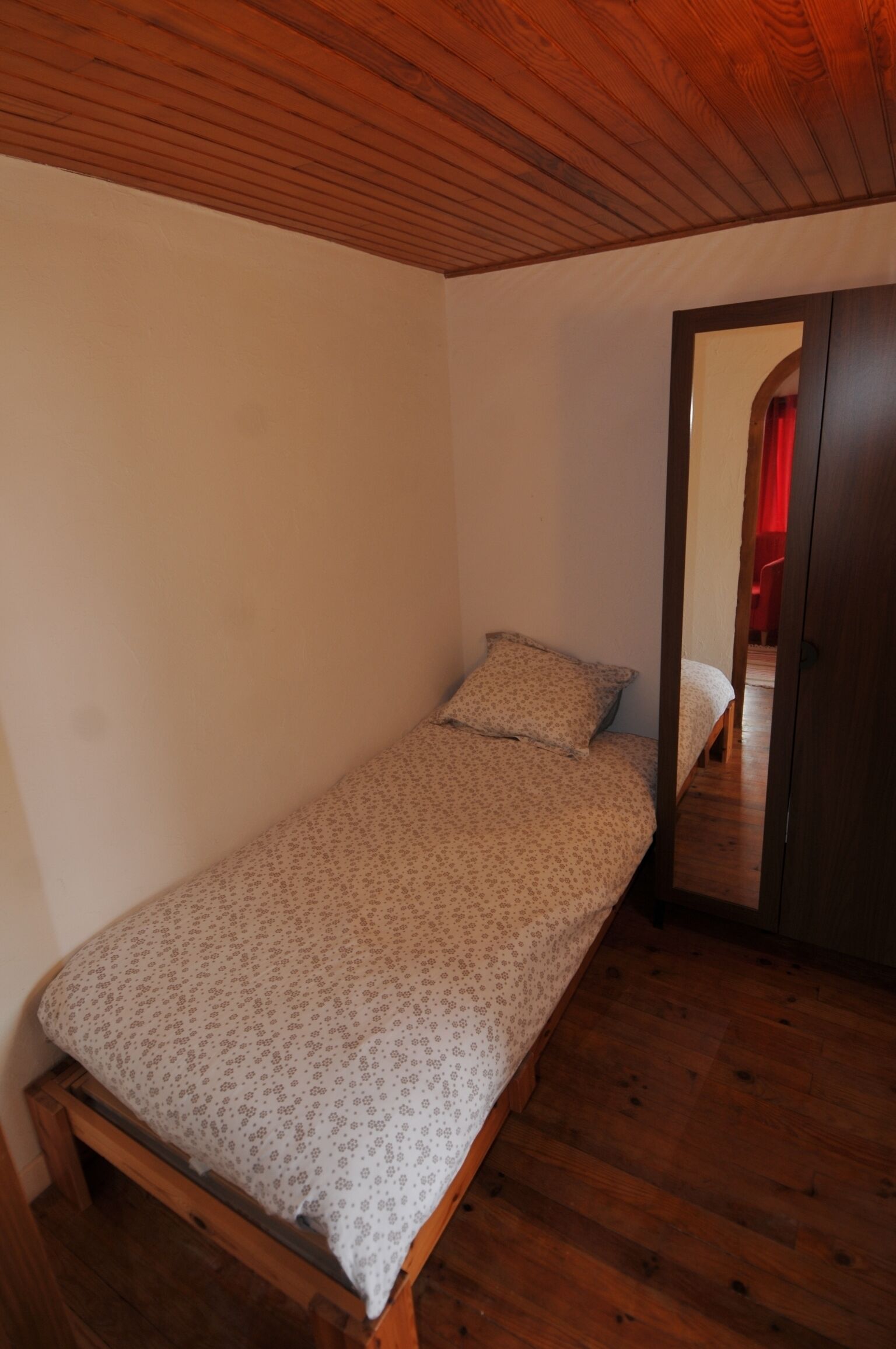 Ein kleines Zimmer mit einem Einzelbett, Holzboden und Holzbalkendecke.