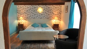 Un dormitorio con una cama, dos lámparas de noche, una mesita redonda y una silla negra.
