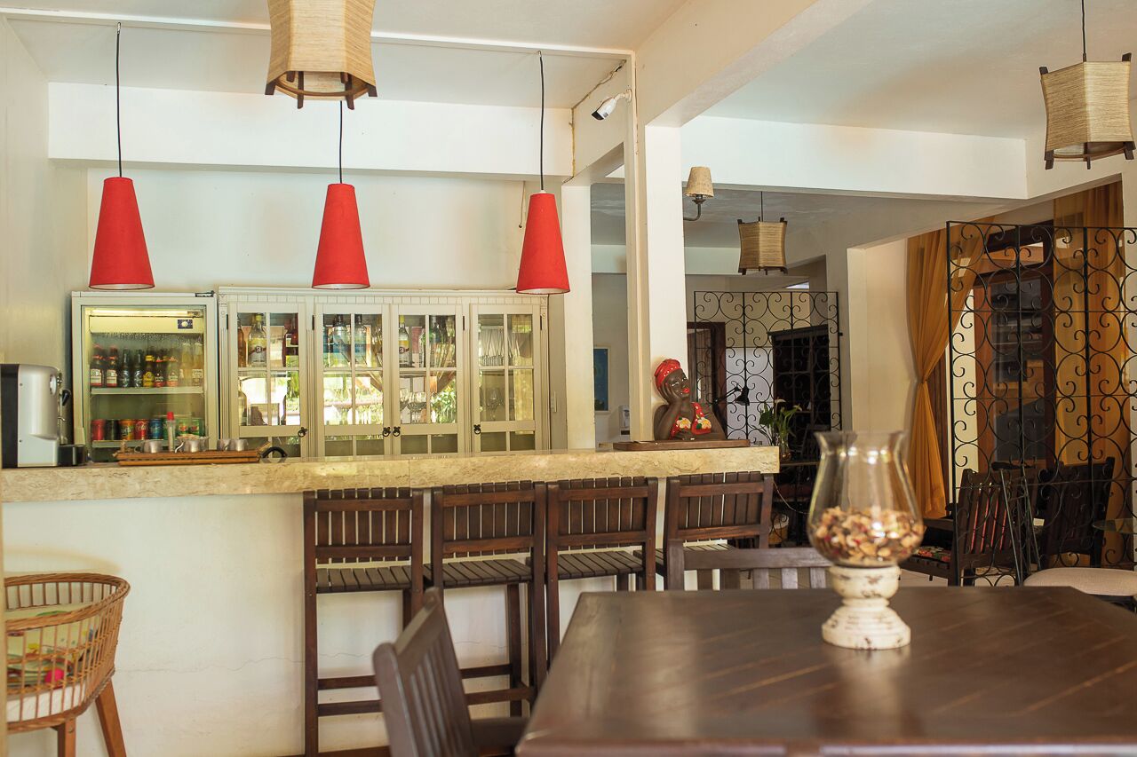 Un comedor con una larga mesa de madera y sillas, una barra con armarios, y lámparas colgantes rojas.