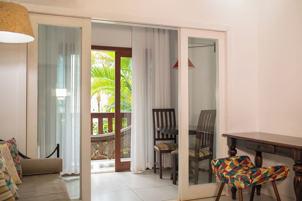 Una habitación con sofá, una mesa de comedor con sillas y vistas a un jardín por una puerta de cristal.
