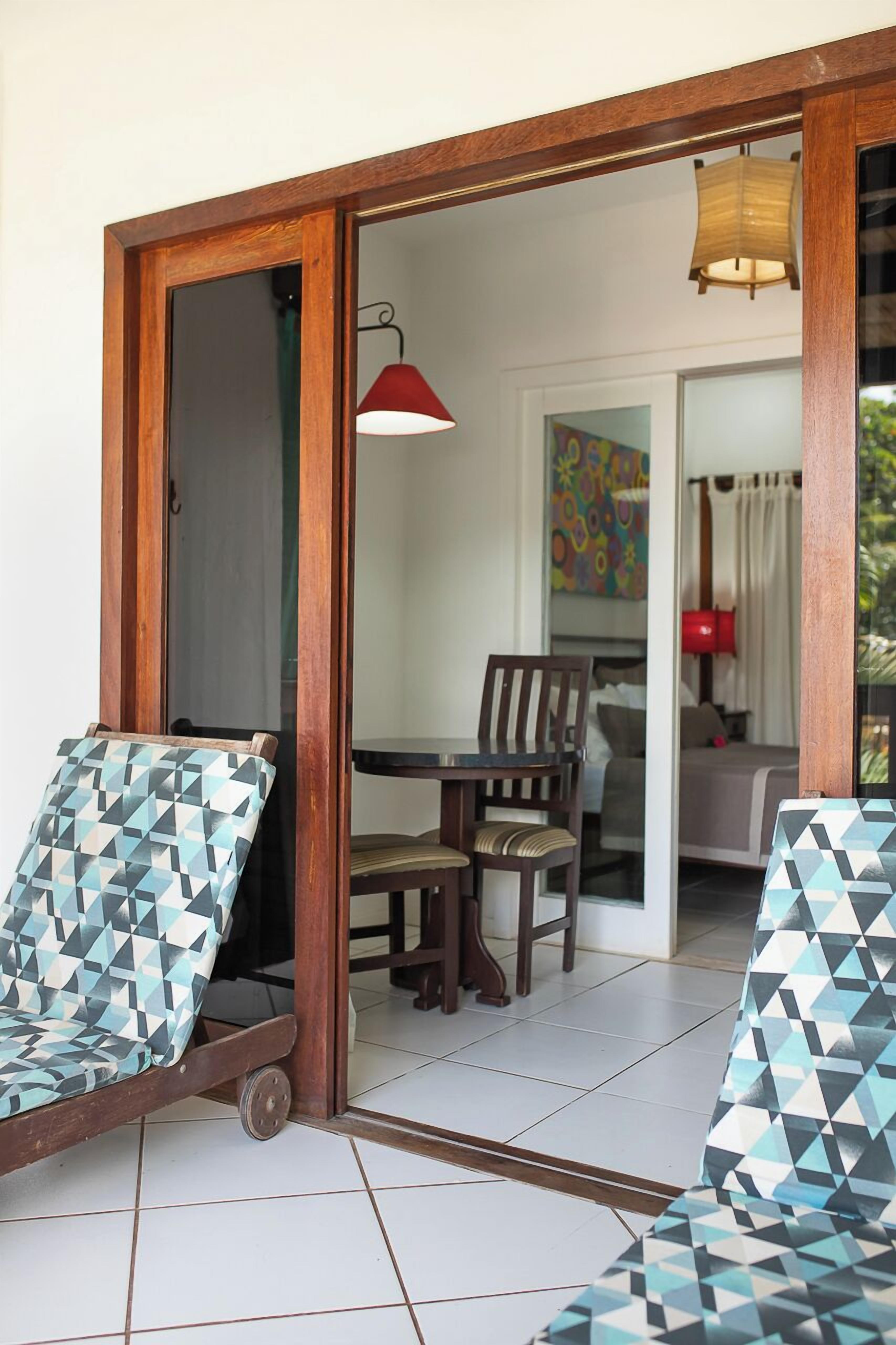 Una habitación con una mesa de comedor y sillas, una cama con cortinas, y vista a un cuadro de colores.