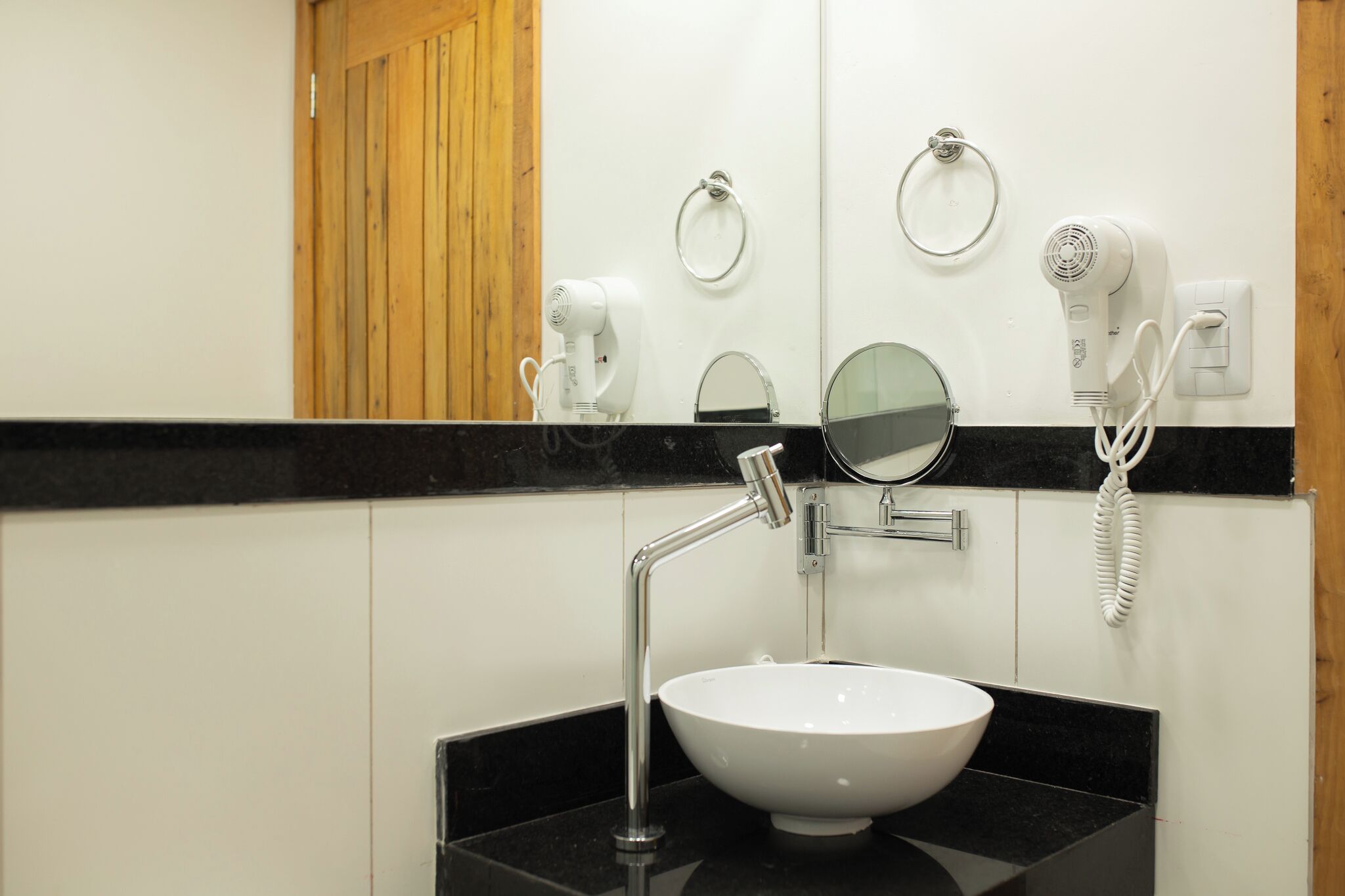 A bathroom with a white sink, a mirror, a towel ring, and two hair dryers.