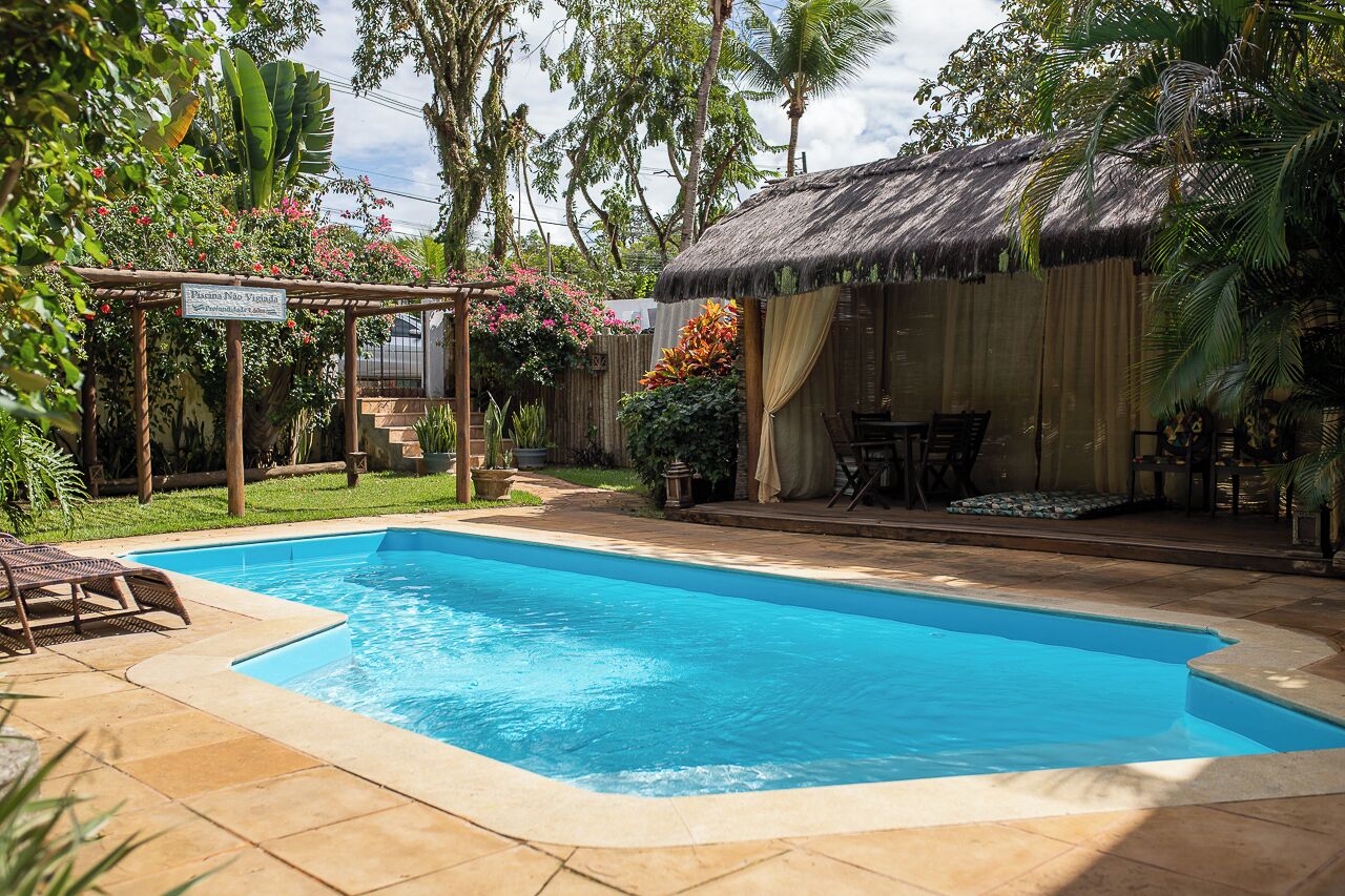 A swimming pool with a pergola, a thatched-roof hut, and lush greenery.