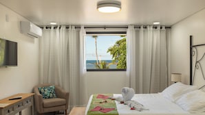 Una habitación de hotel con cama, una silla, un escritorio, televisión y ventana con vista al océano.