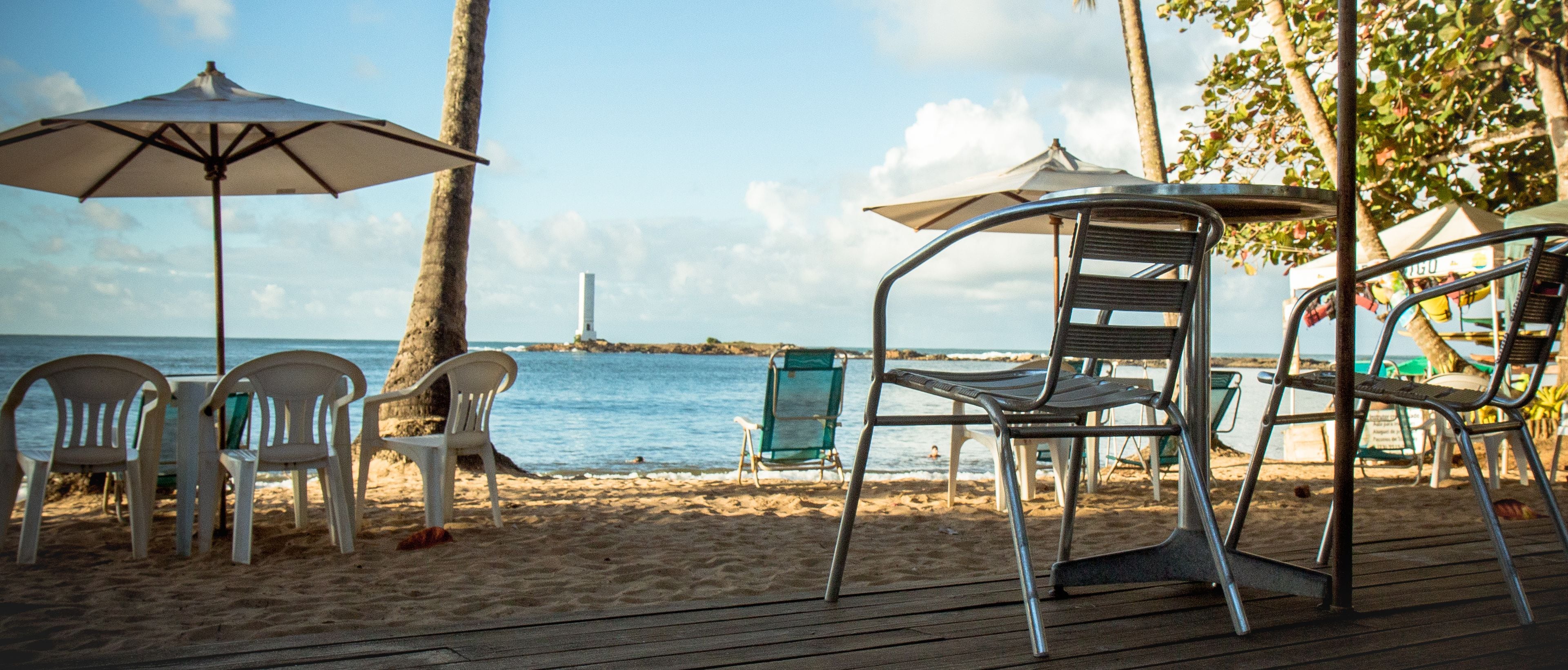 A beachside seating area with plastic chairs and umbrellas, overlooking the sea.
