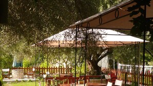 An outdoor seating area with wooden tables and chairs, surrounded by a wooden fence and potted plants. - Avra Hotel (Lefkada)
