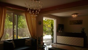 A living room with a sofa, a glass coffee table, and a chandelier. There is a door leading to an outdoor area with plants. - Avra Hotel (Lefkada)