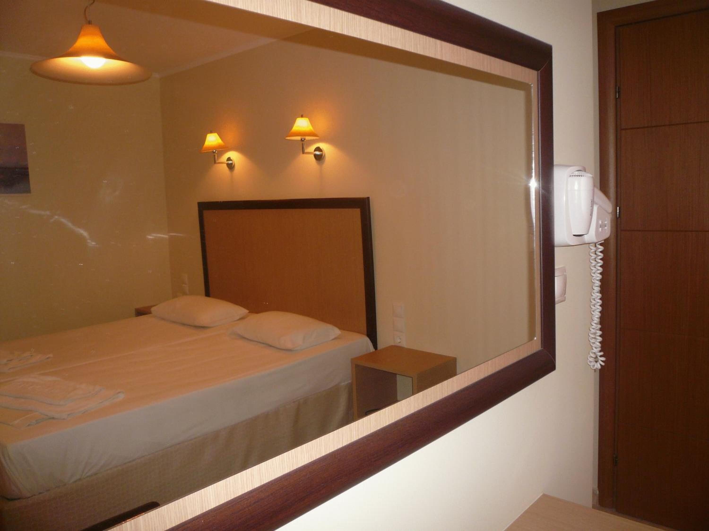 A hotel room with a bed, bedside lamps, a telephone, and a mirror reflecting the room.