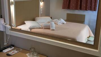 A hotel room with a large mirror above a bed, a bedside table with a phone, a glass, and a vase of flowers.