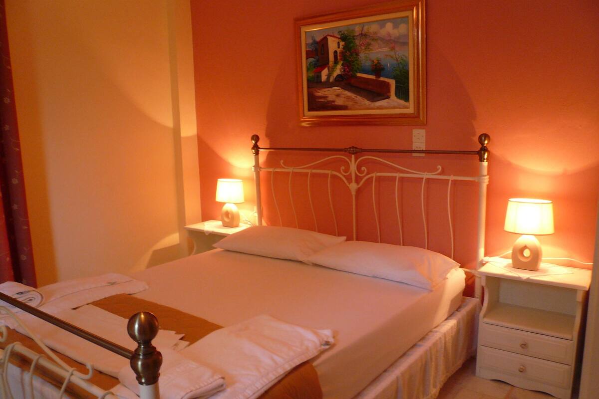 Un letto rifatto con lenzuola bianche e una testiera in legno, due comodini con lampade e un quadro appeso alla parete.