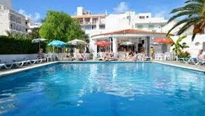 A swimming pool with lounge chairs and umbrellas, surrounded by buildings and greenery. - Apartamentos Tramuntana (Sant Antoni de Portmany)