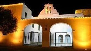A building with a traditional architectural style, featuring arched doorways and a central tower. - Apartamentos Tramuntana (Sant Antoni de Portmany)