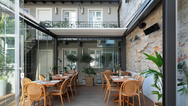 Ein Essbereich mit Holztischen und -stühlen, Blumentöpfen und einer Steinwand.