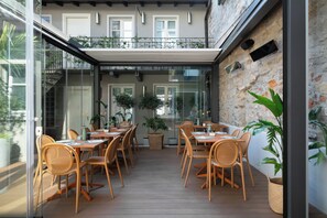 A dining area with wooden tables and chairs, potted plants, and a stone wall. - Avenue Boutique Hotel (Como)