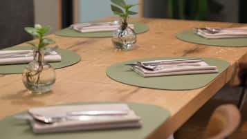 Een houten eettafel met groene placemats, netjes gevouwen witte servetten en twee glazen vazen met planten.