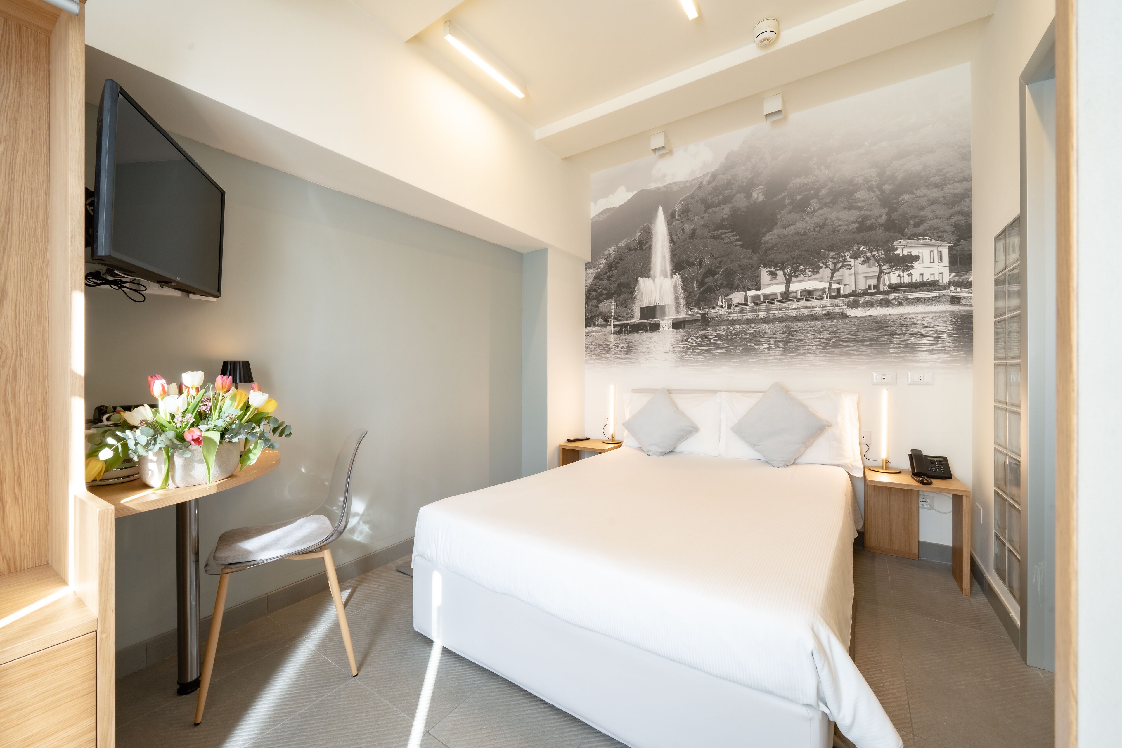 Een moderne hotelkamer met een groot bed, een bureau met een stoel, een flatscreen-televisie en een wandkunstwerk van een fontein.