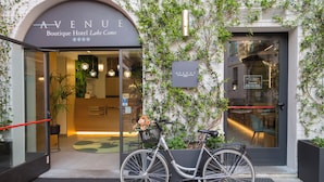 Der Eingang zum Avenue Boutique Hotel am Comer See, mit einem Fahrrad, einem Blumentopf und einem Schild.