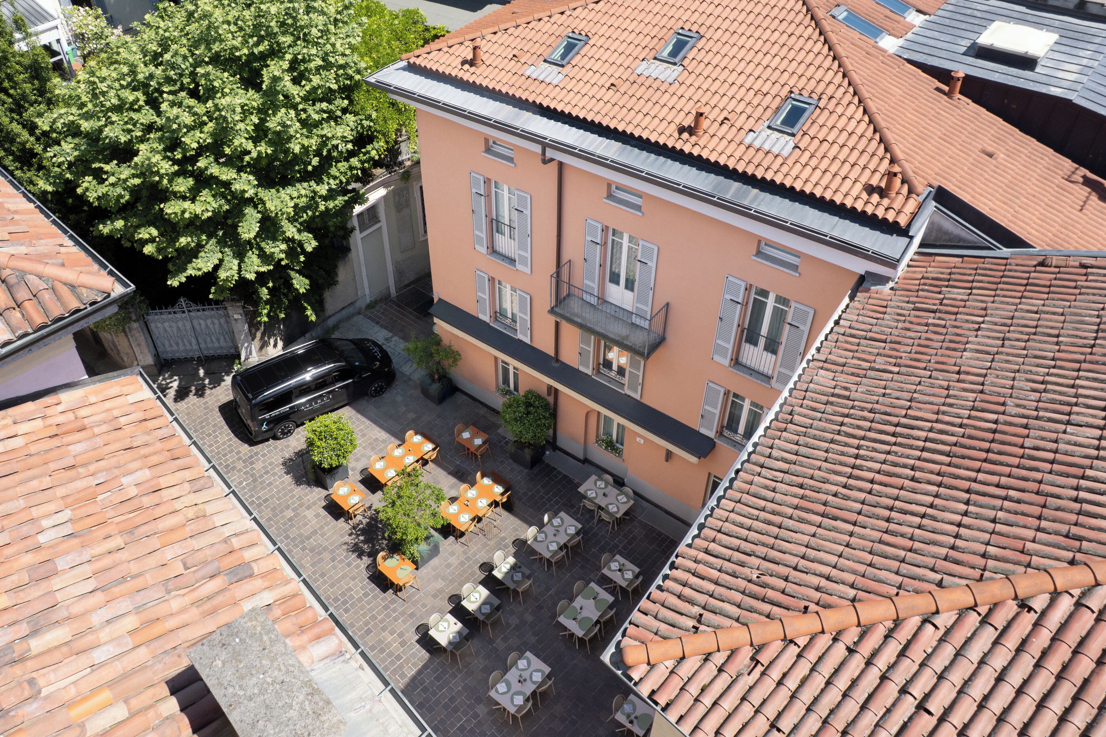 A courtyard with outdoor seating, a car, and a building with a tiled roof and shutters.