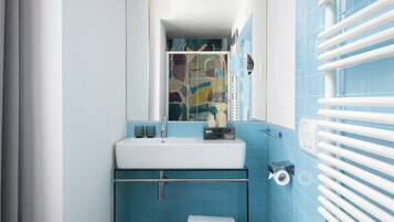 Un baño con un lavamanos blanco, azulejos azules, una cabina de ducha de vidrio y un perchero para toallas.