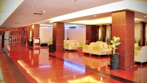 A hotel lobby with a polished red floor, white sofas with green cushions, and a large potted plant. - Pandanaran Hotel Semarang (Semarang)