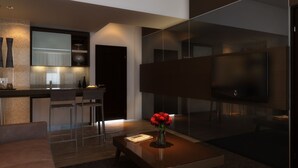 A modern living room with a flat-screen TV, a coffee table with a vase of flowers, and a dining area with chairs and a kitchen in the background. - Pandanaran Hotel Semarang (Semarang)