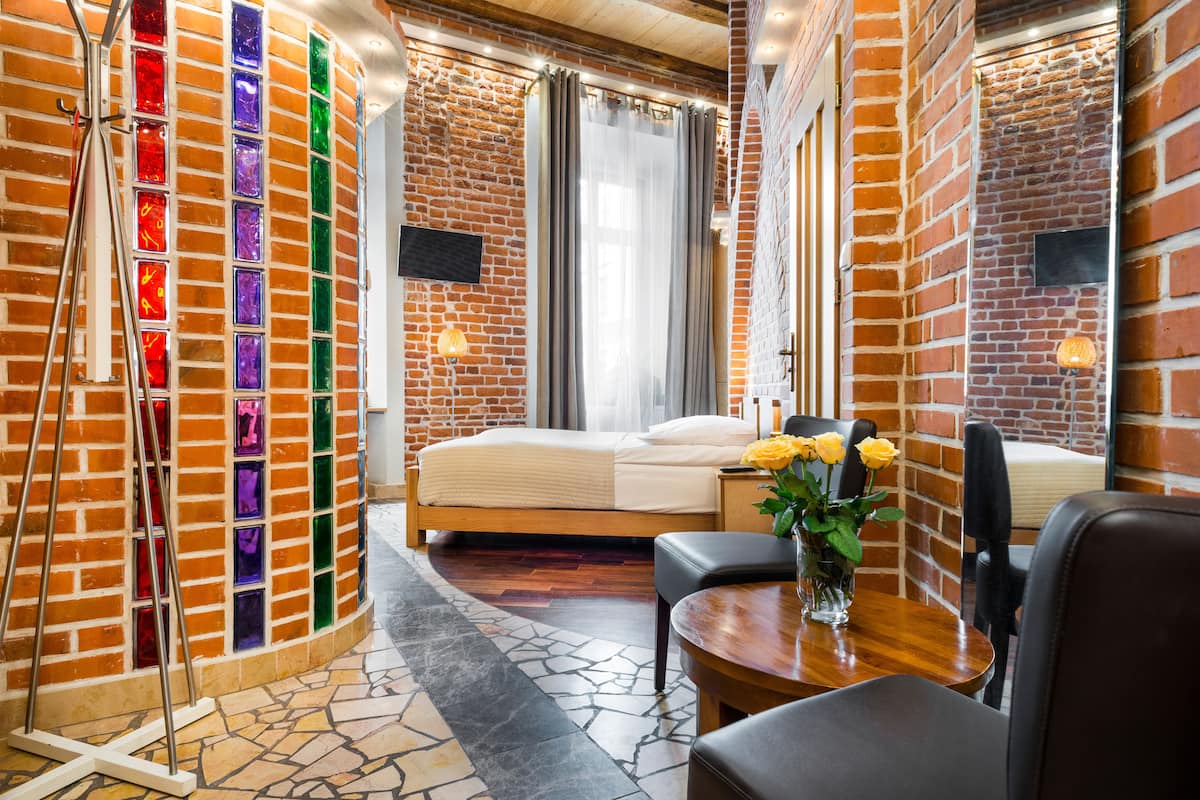 A hotel room with a brick wall, a bed, a desk, and a chair.