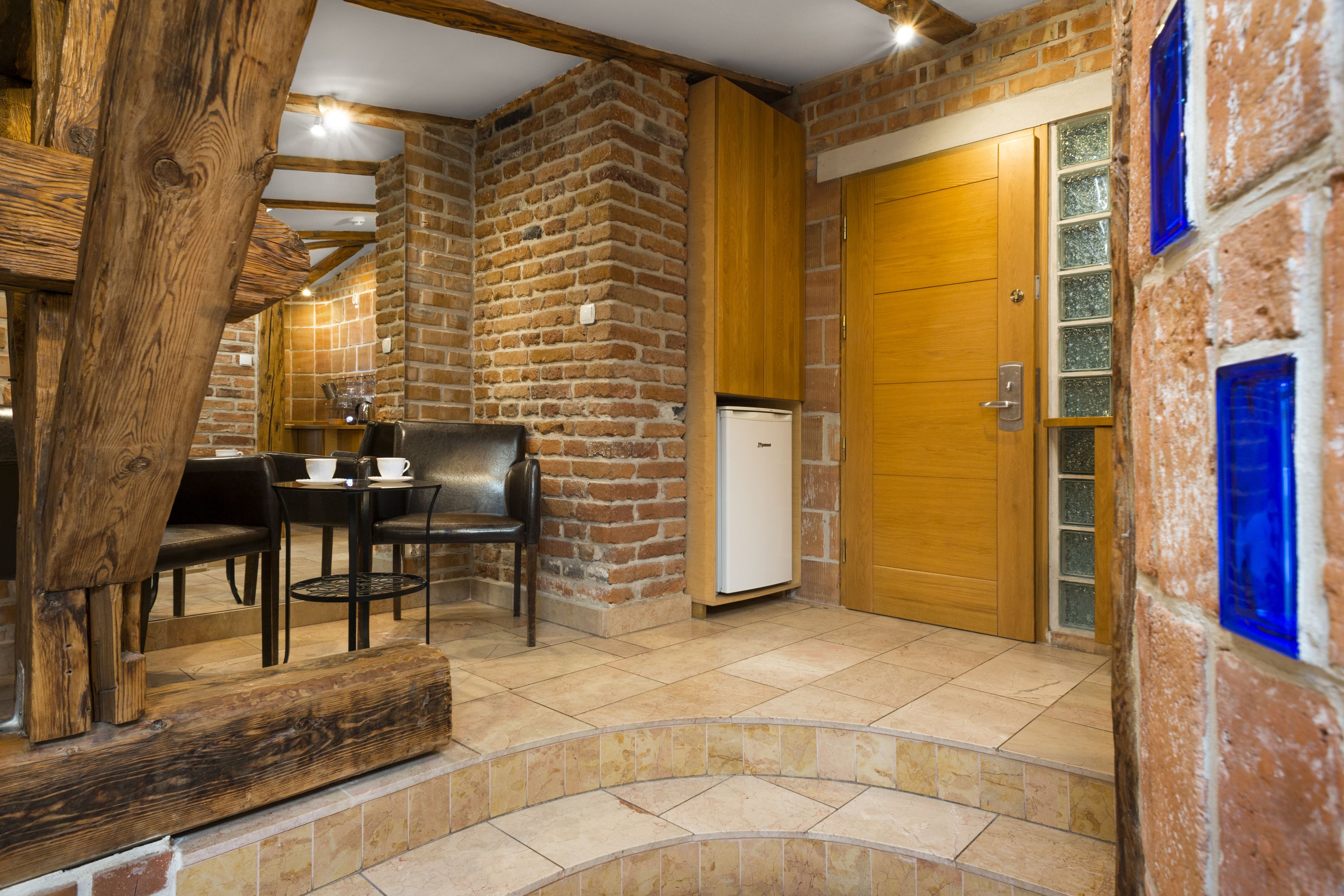 A rustic interior with exposed brick walls, a wooden door, and a small table with chairs.