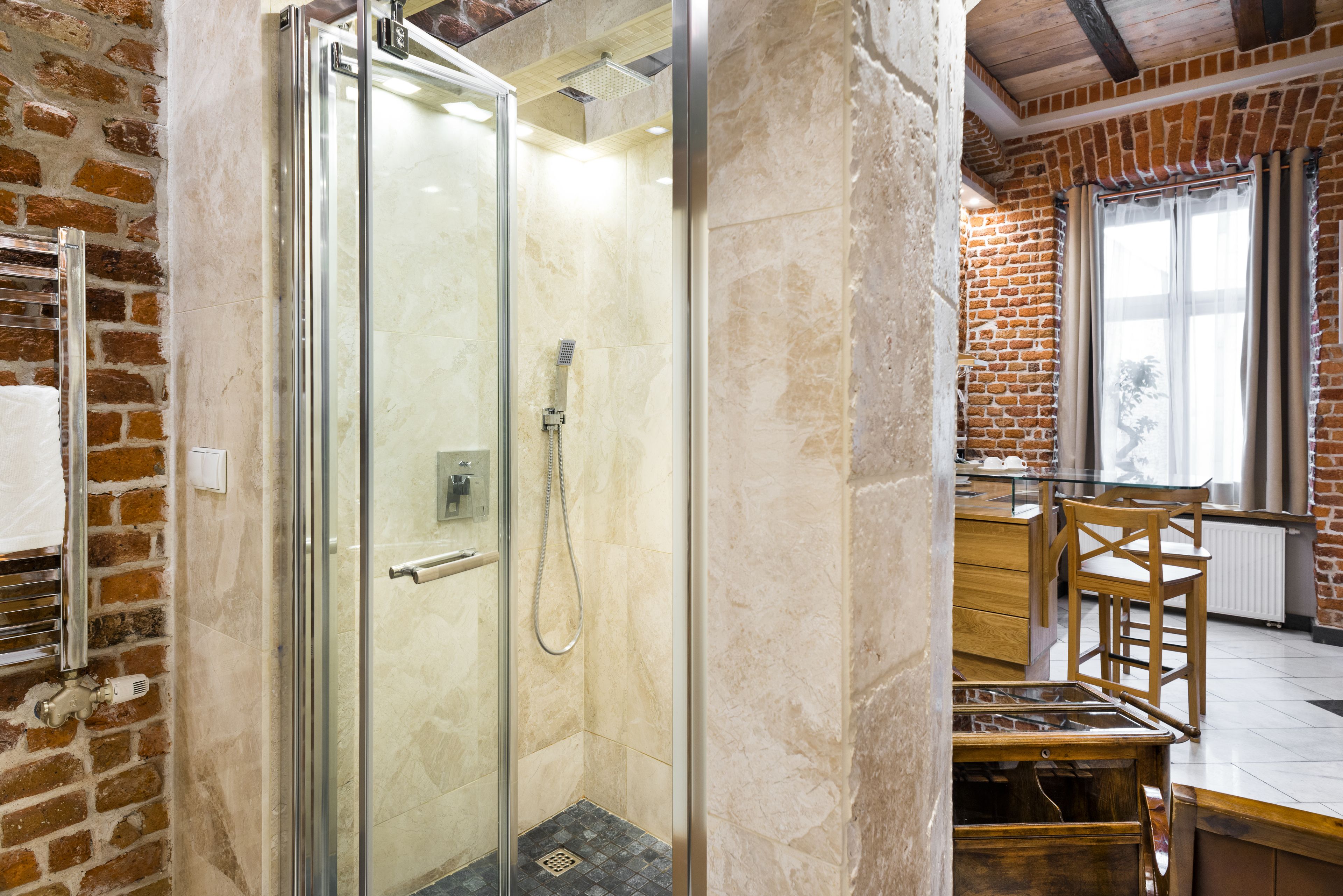 Ein modernes Badezimmer mit einer Glaskabinentrennung zur Dusche, einer Holzbank und einer Ziegelwand.