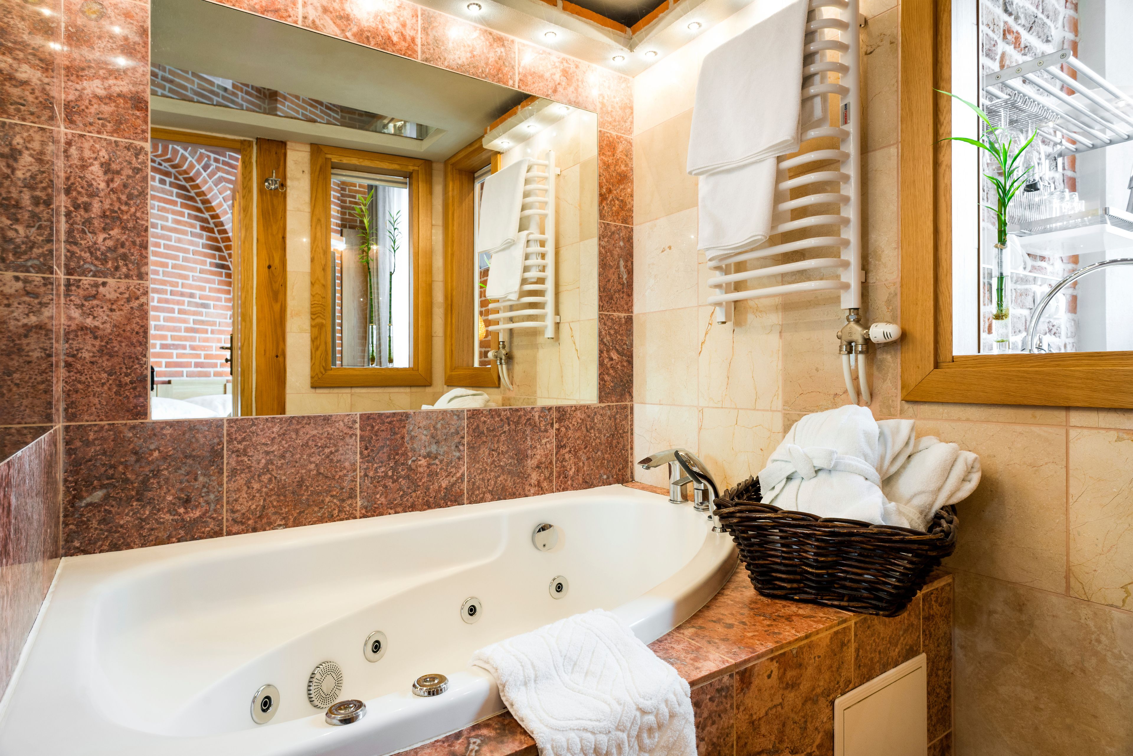 A modern bathroom with a large bathtub, a wooden door, and a mirror reflecting the room.