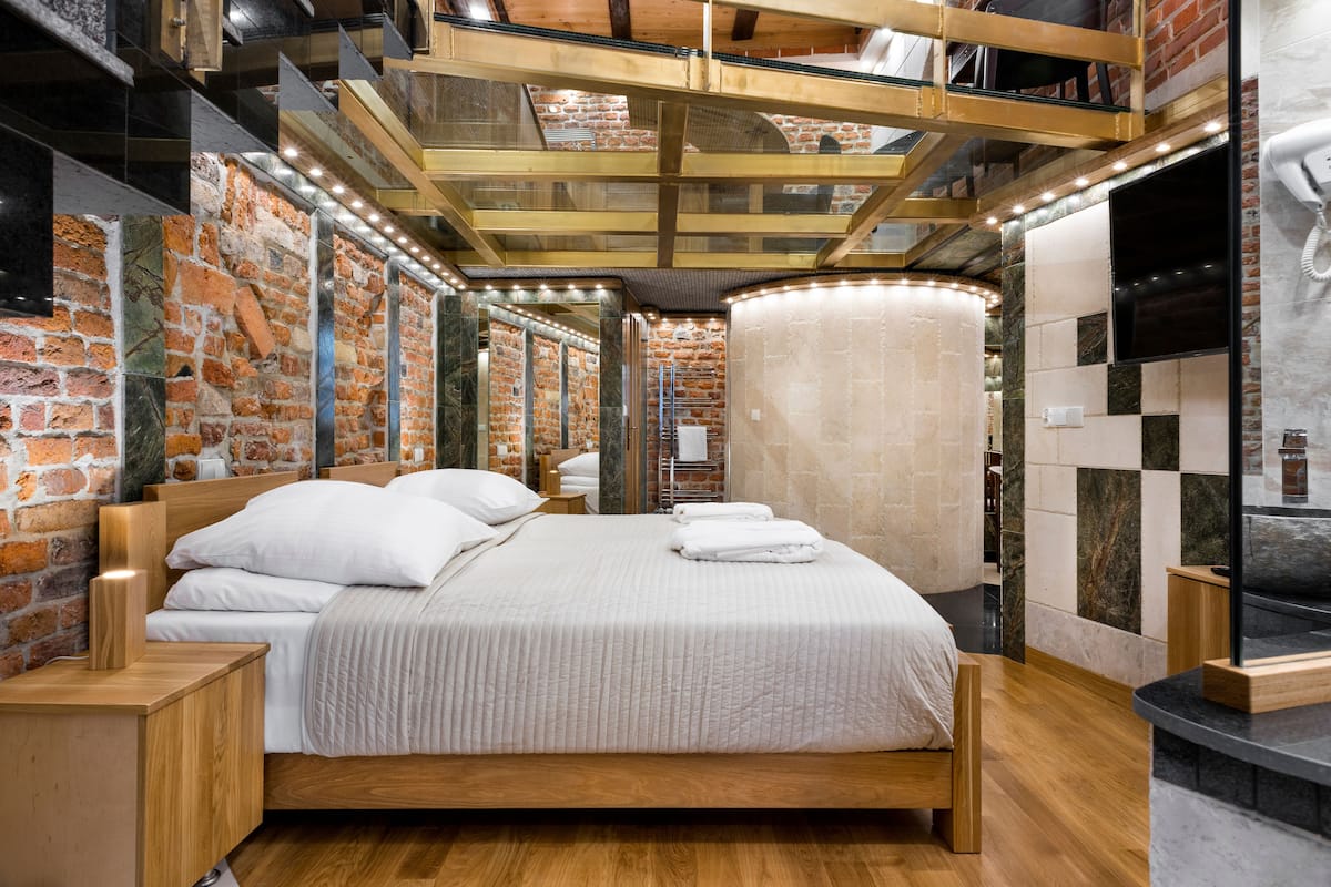 A modern hotel room with a brick wall, a wooden bed, and a large window.