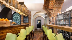 A bar area with wooden bar counters, green chairs, and a brick wall. - Aparthotel Stare Miasto (Kraków)