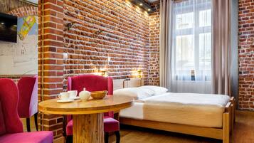 Una habitación con pared de ladrillo, una cama, una mesa redonda de madera con sillas y un televisor en la pared.