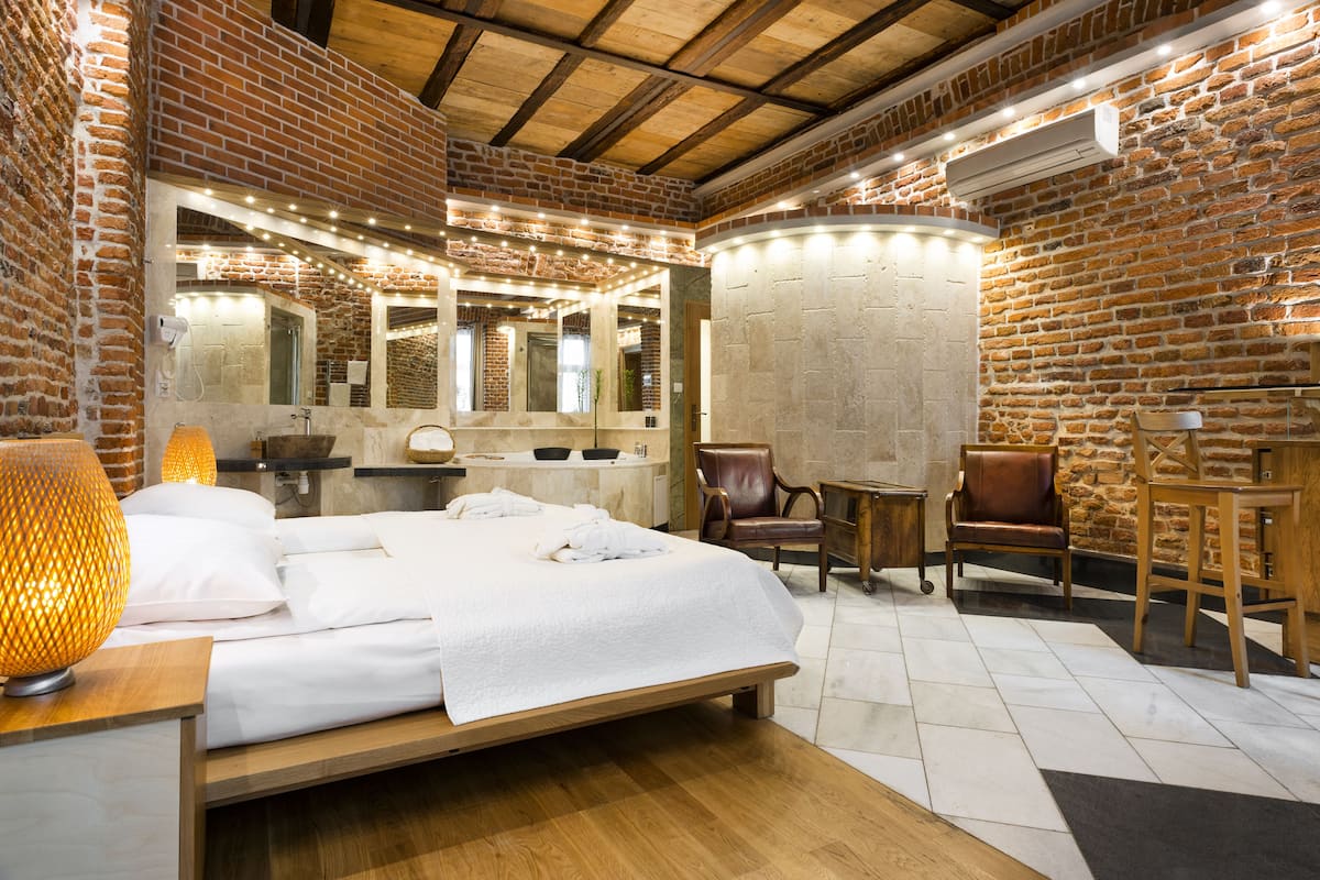 A hotel room with a brick wall, a wooden ceiling, a large bed, a desk, and a chair.