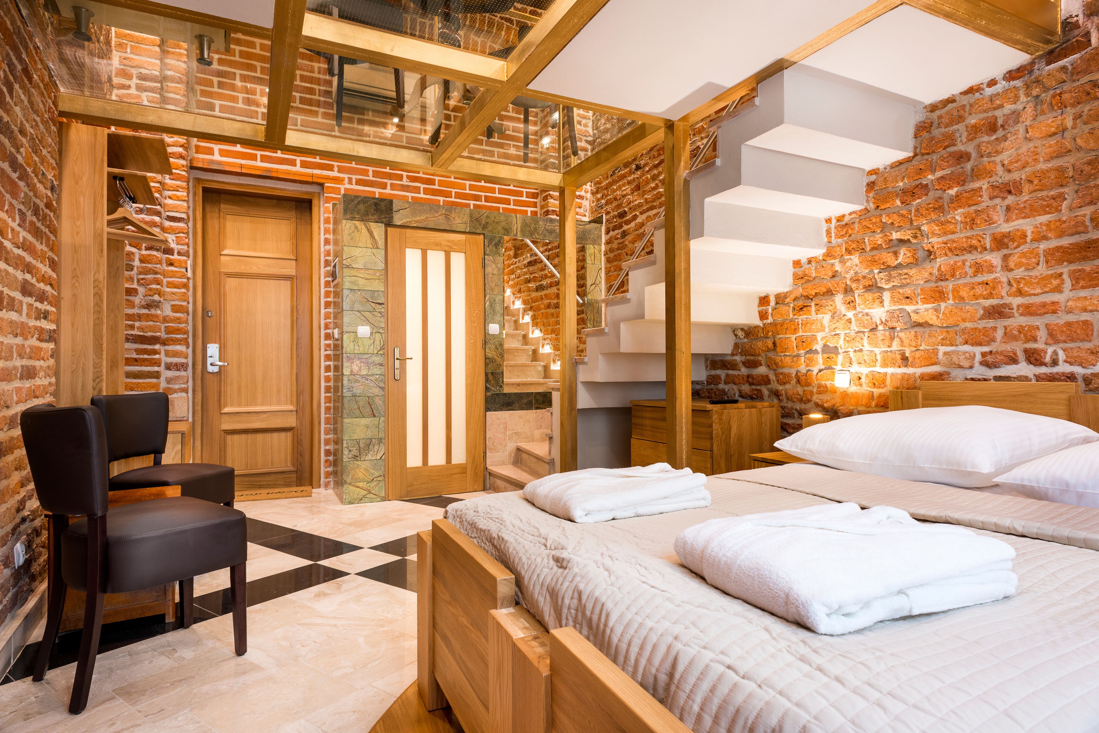 A modern hotel room with a brick wall, a wooden bed, a chair, and a staircase.