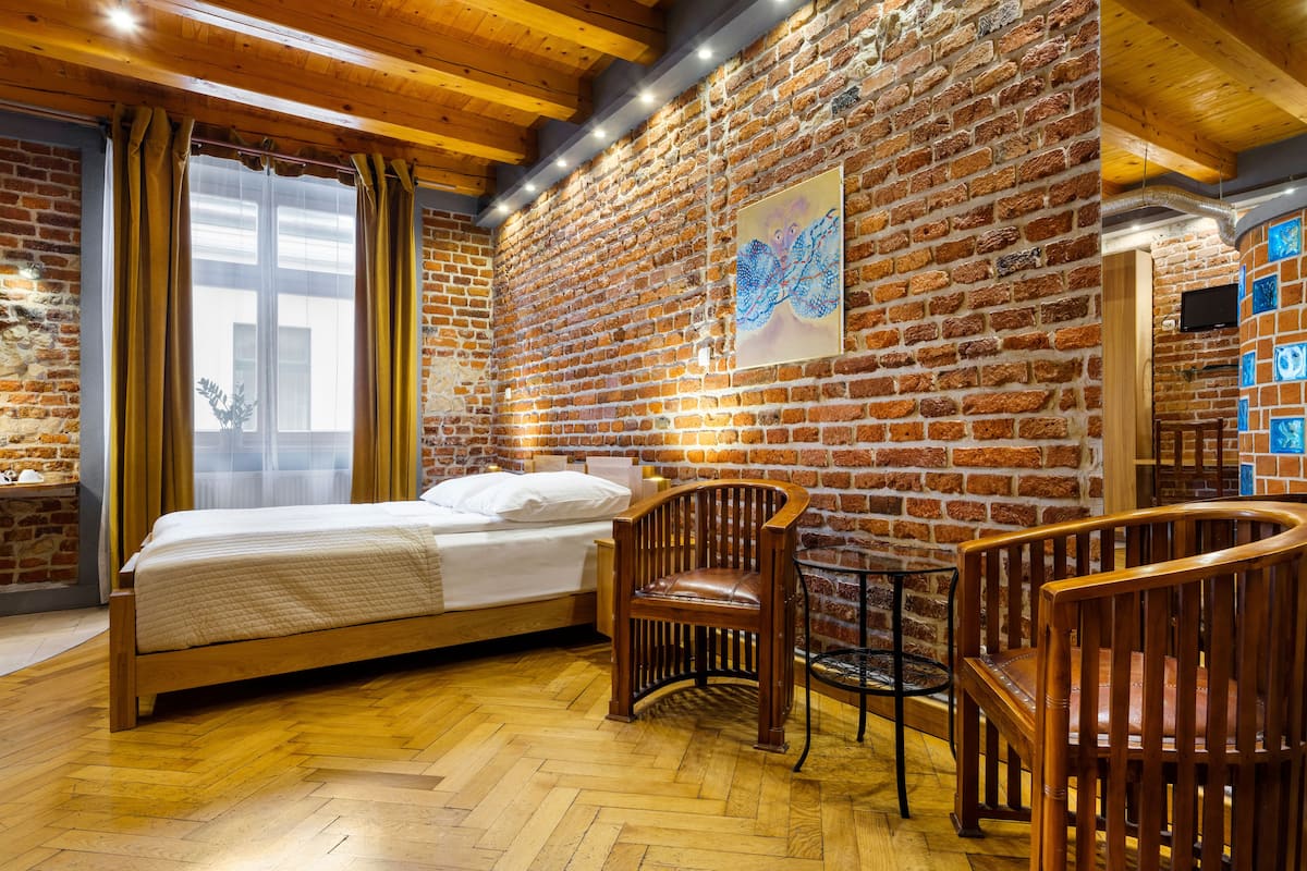 A room with a brick wall, wooden ceiling beams, a bed, a chair, and a table.