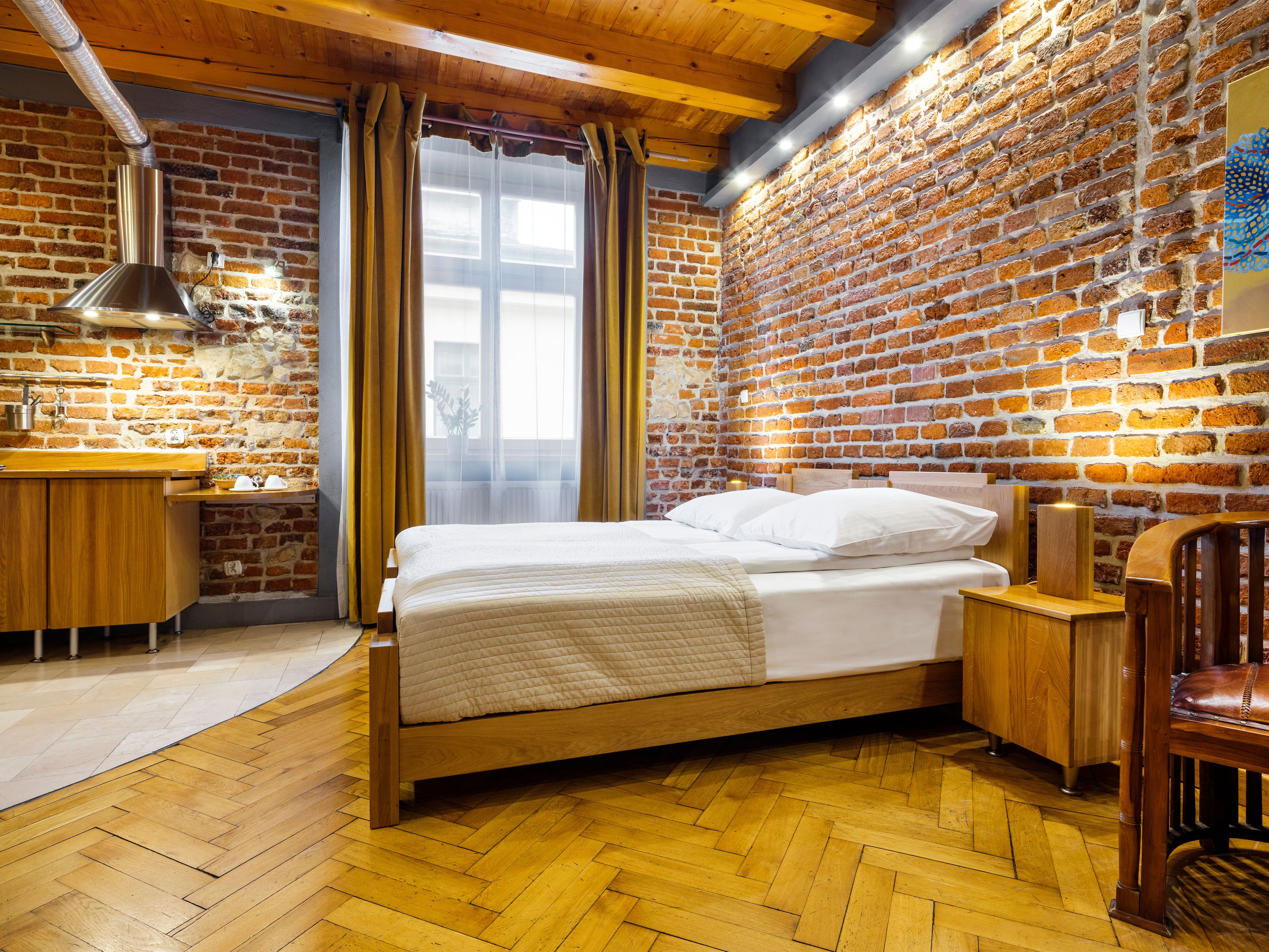 A bedroom with a wooden bed, a brick wall, a wooden dresser, and a window with curtains.