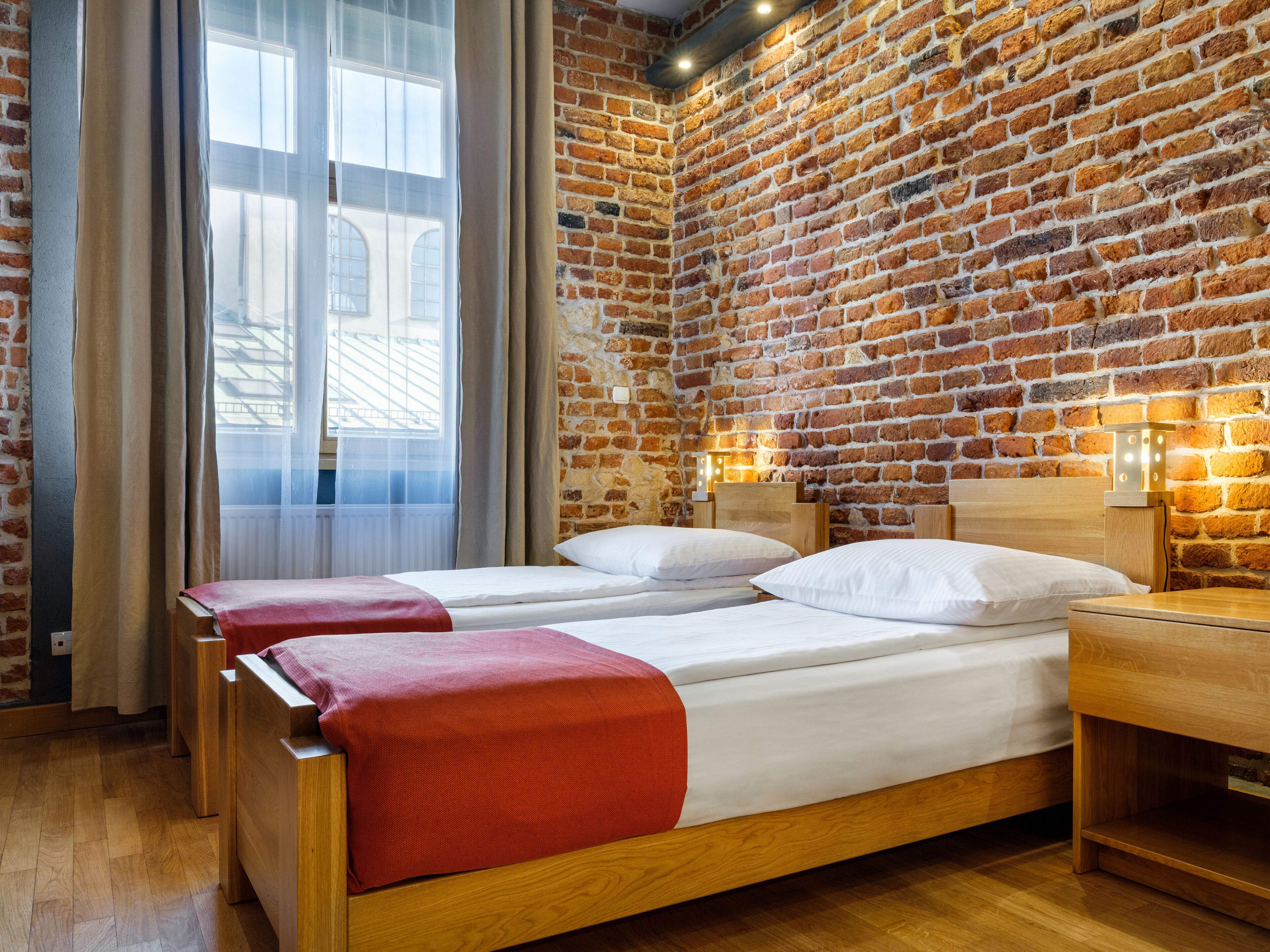 Quarto com duas camas de madeira, uma parede de tijolos e uma janela com cortinas.