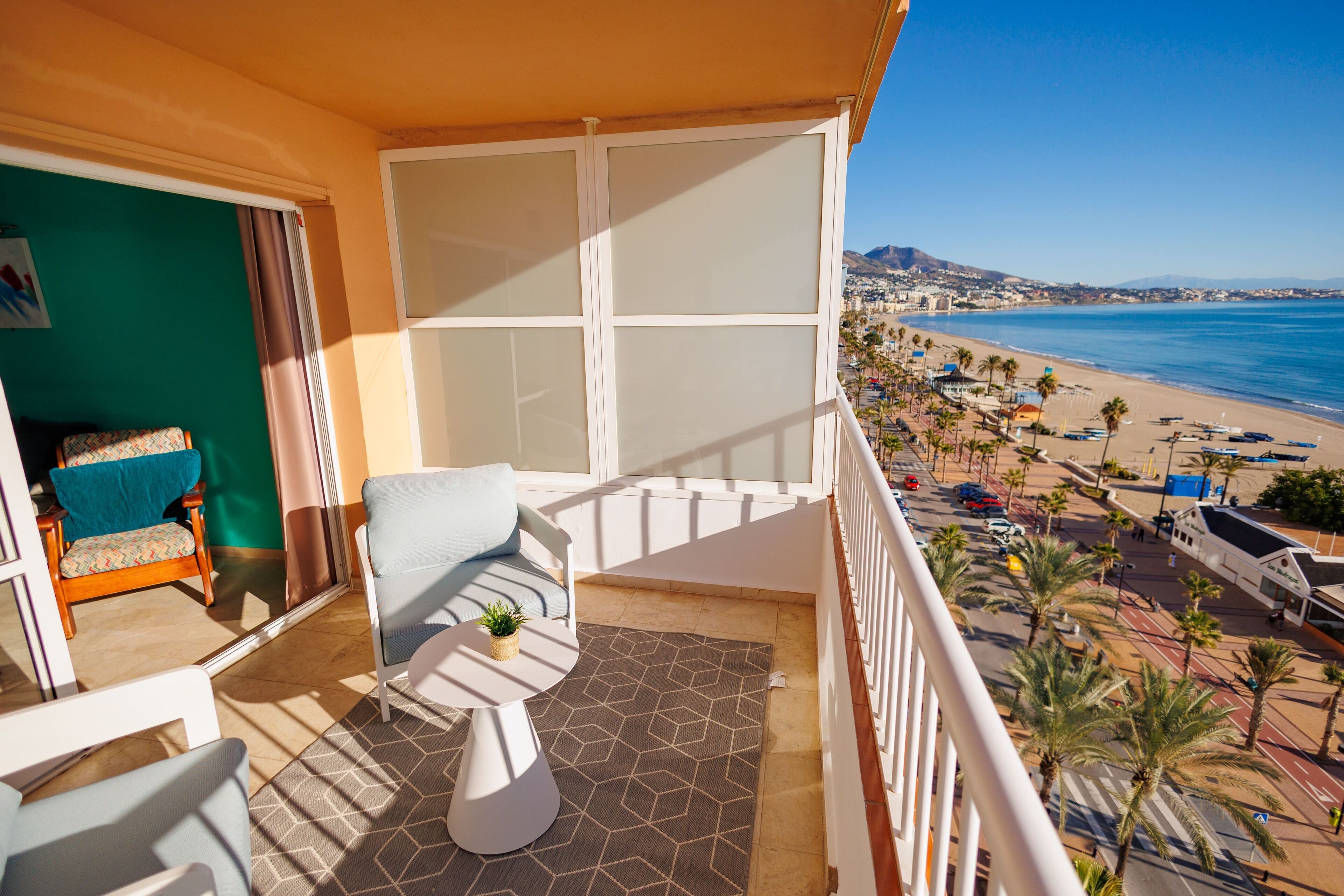 A balcony with a view of the beach, a chair, a small table, and a plant.