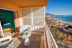 A balcony with a view of the beach, a chair, a small table, and a plant.