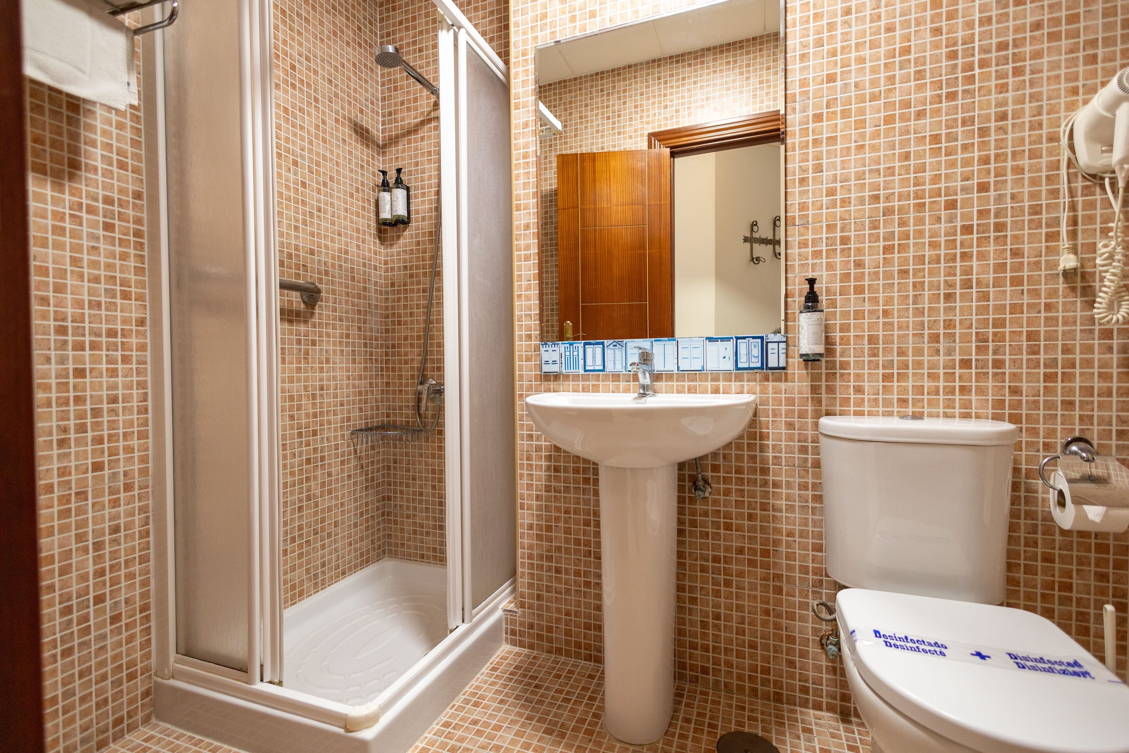 A bathroom with a shower, sink, and toilet, featuring tiled walls and a mirror.