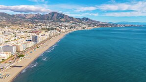 Un paisaje costero con una playa, edificios y montañas al fondo.