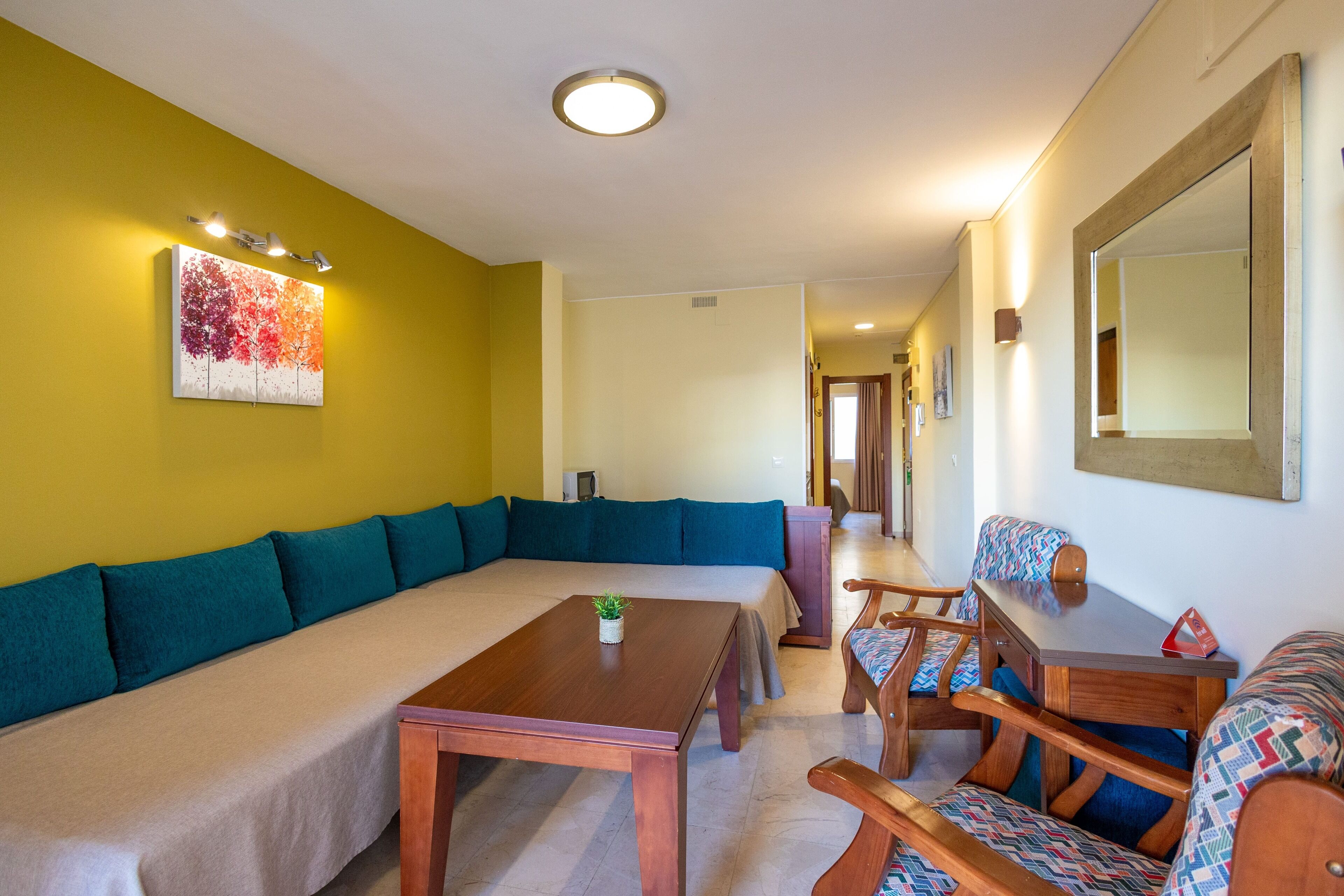 Una habitación con un sofá, una mesa de madera y una silla. Hay un cuadro en la pared y un espejo sobre la mesa.
