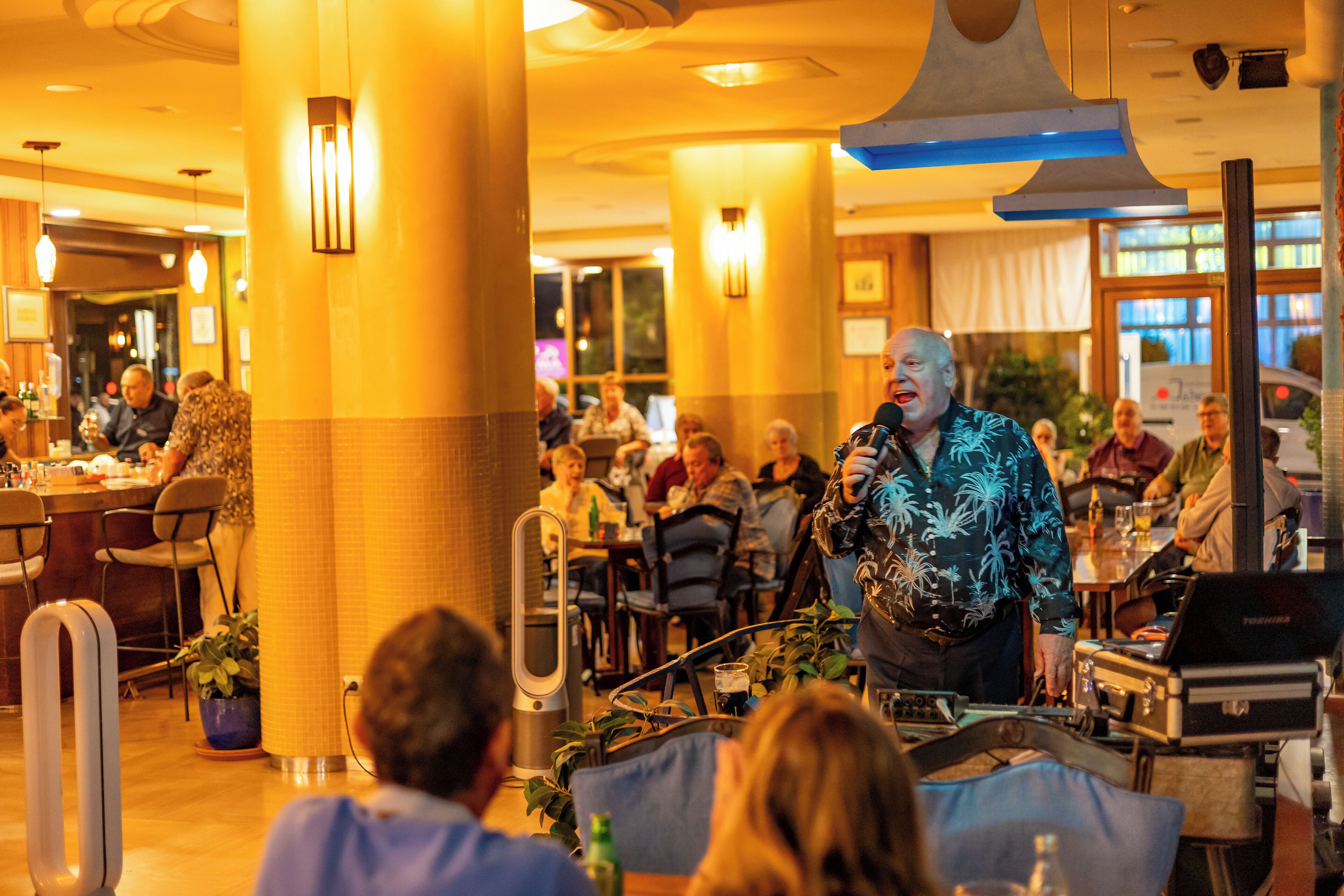 A hotel lobby with a stage for performances, dining tables, and chairs.