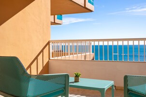 Un balcon avec deux chaises vertes, une petite table et un pot de fleurs.