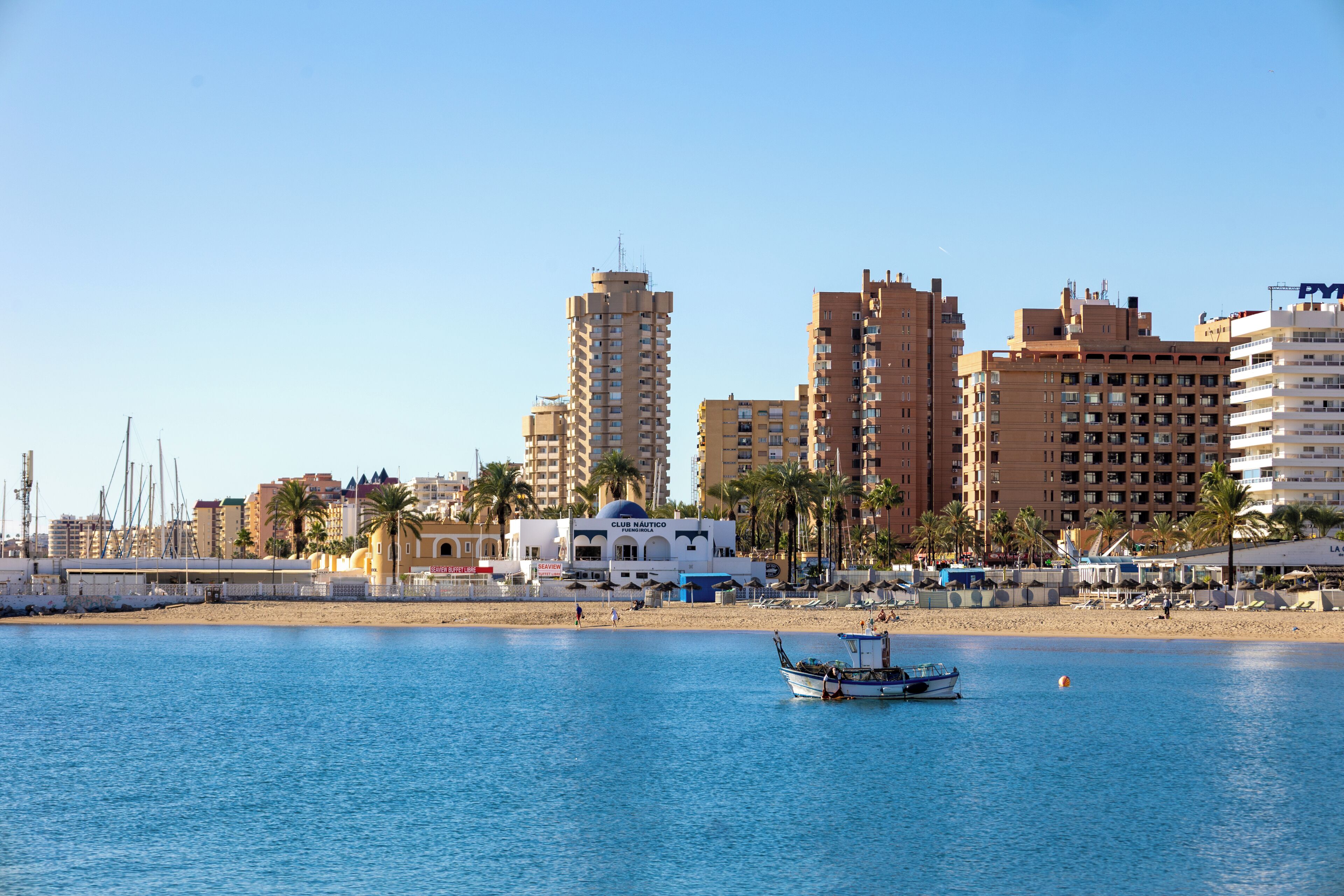 Un paisaje urbano costero con edificios altos, una playa y un barco en el agua.