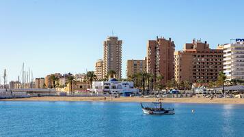 Un paisaje urbano costero con edificios altos, una playa y un barco en el agua.