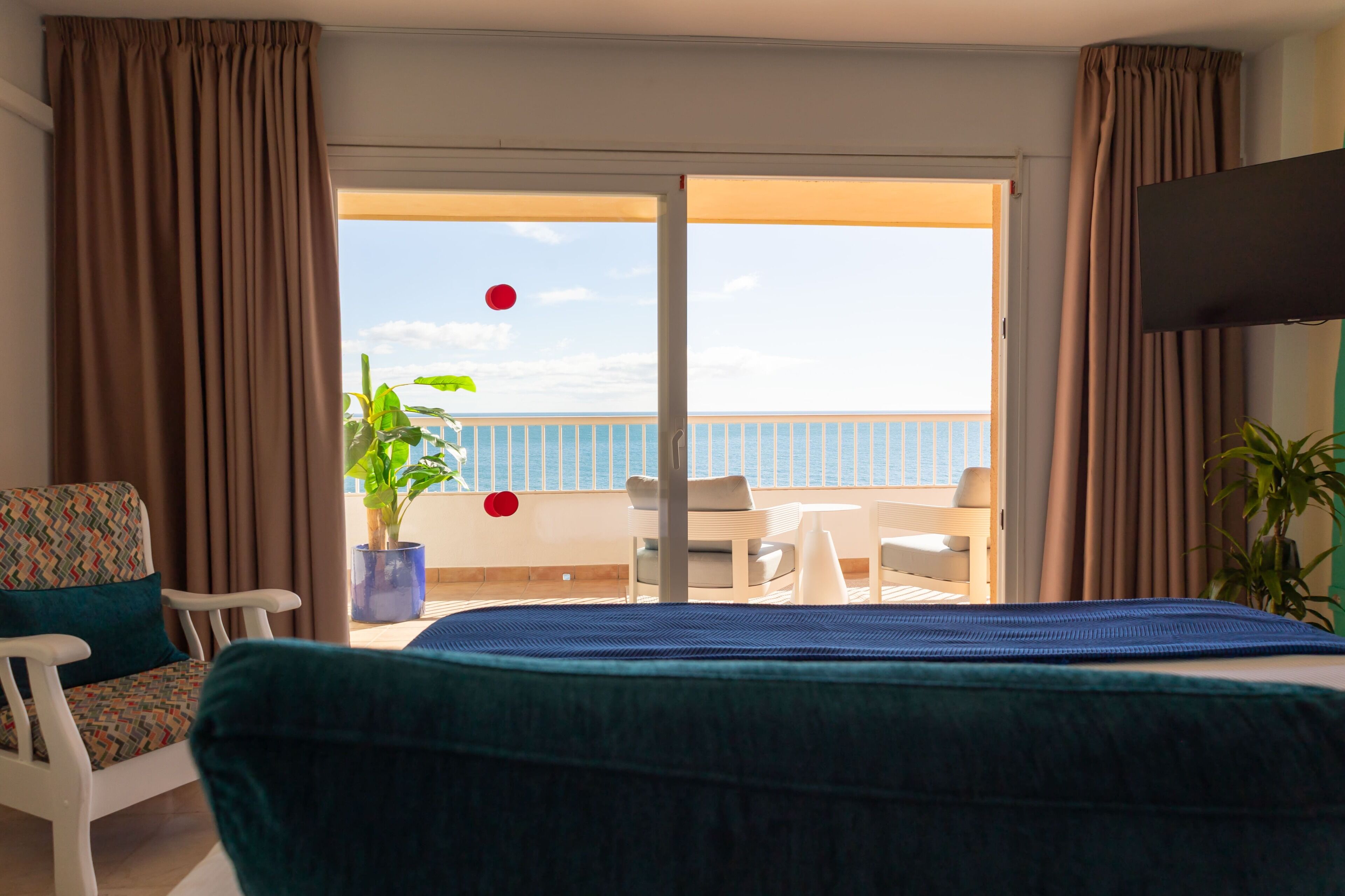 A hotel room with a bed, a chair, a table, and a potted plant.