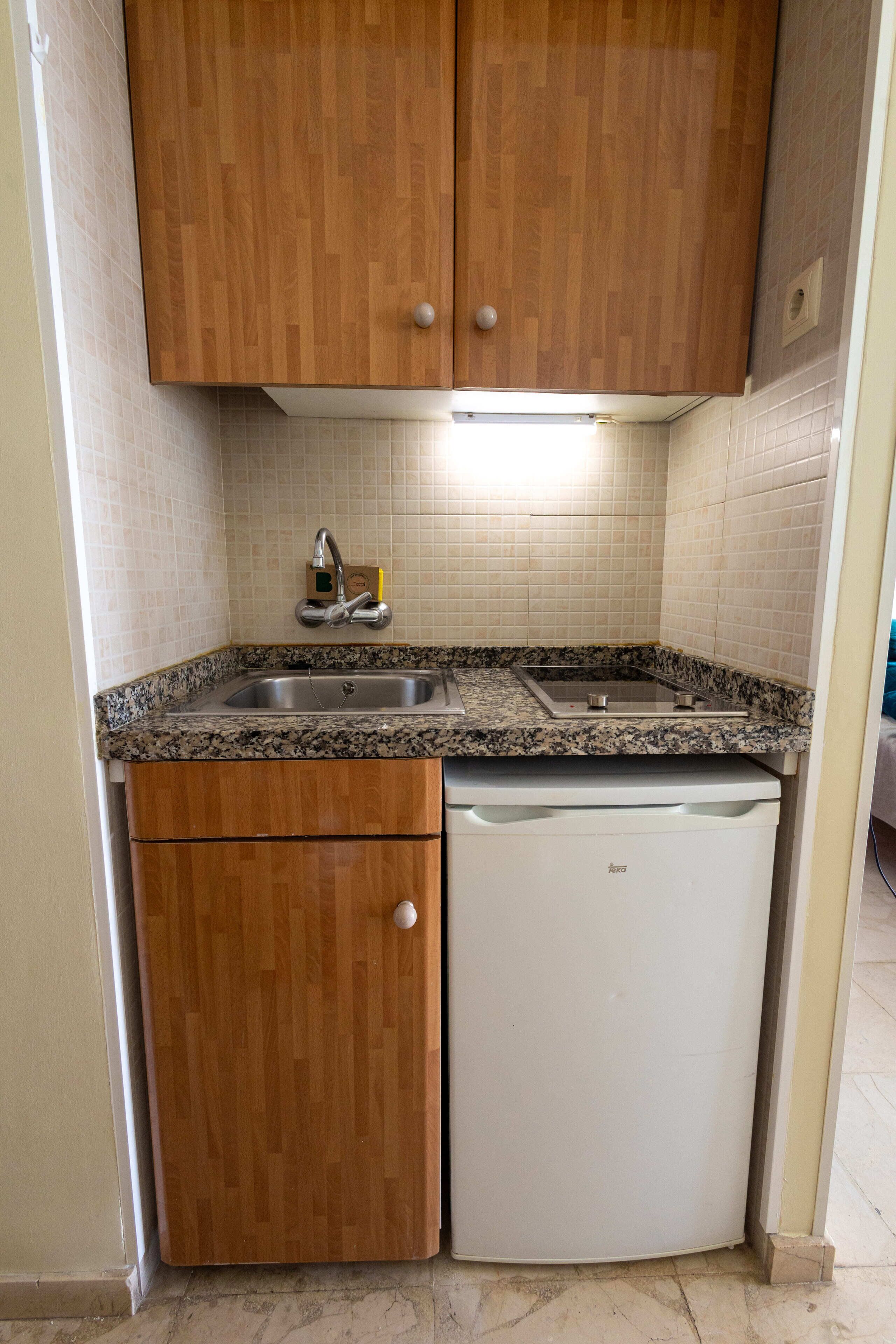 A compact kitchen with wooden cabinets, a granite countertop, a built-in dishwasher, and a stainless steel sink.