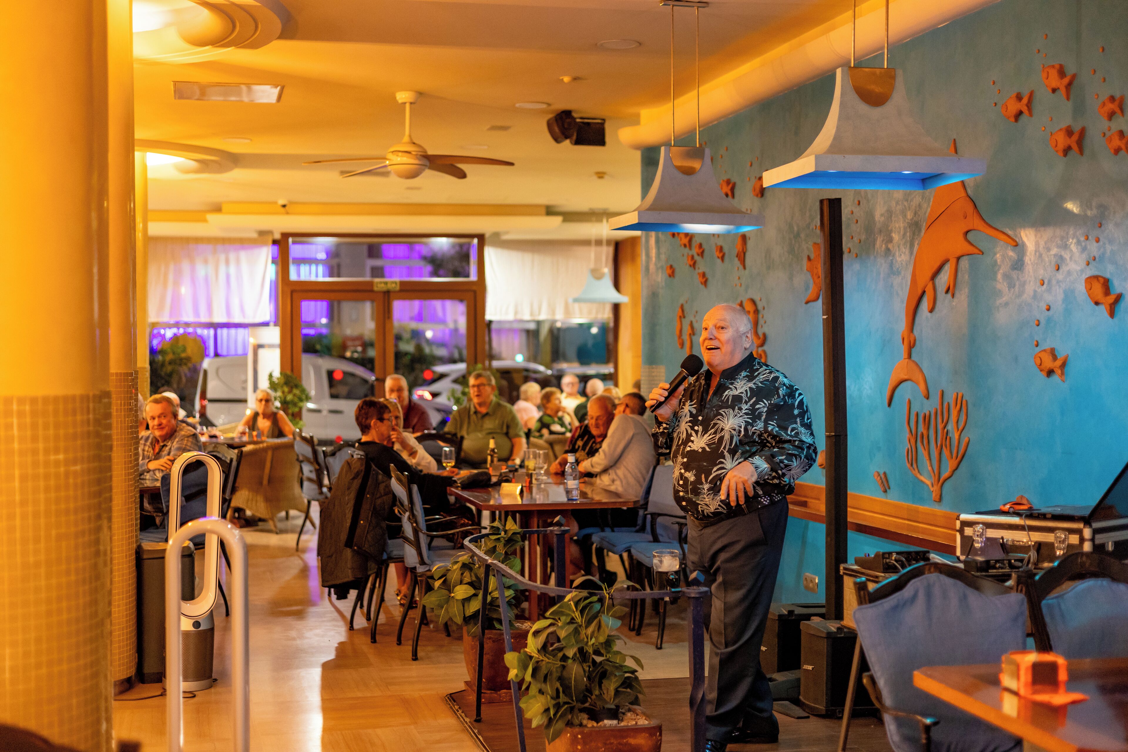 L’intérieur d’un restaurant, avec des tables, des chaises, des ventilateurs de plafond et des œuvres d’art décoratives sur les murs.