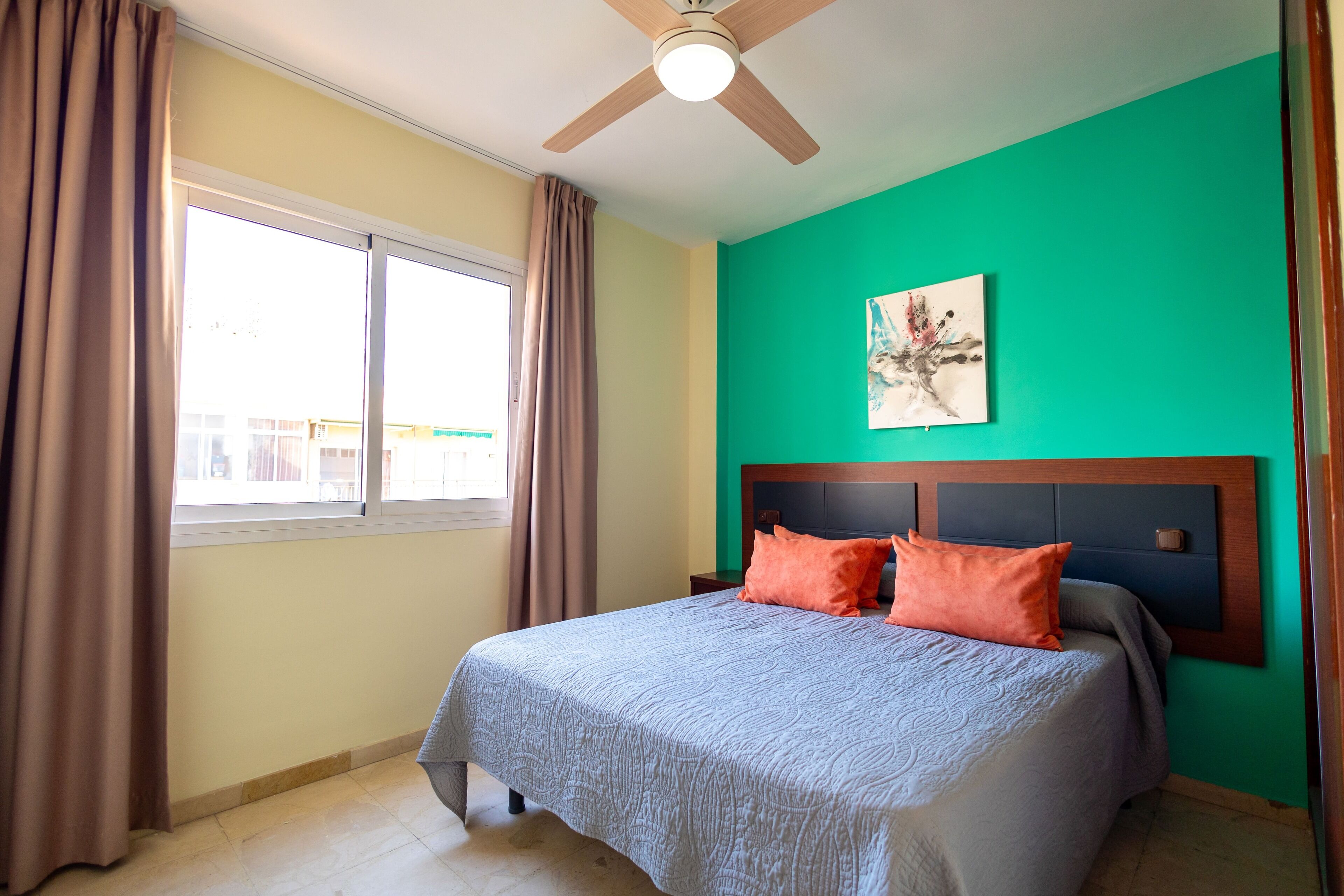 Ein Schlafzimmer mit Bett, Deckenventilator, Fenster mit Vorhängen und einer grünen Wand.